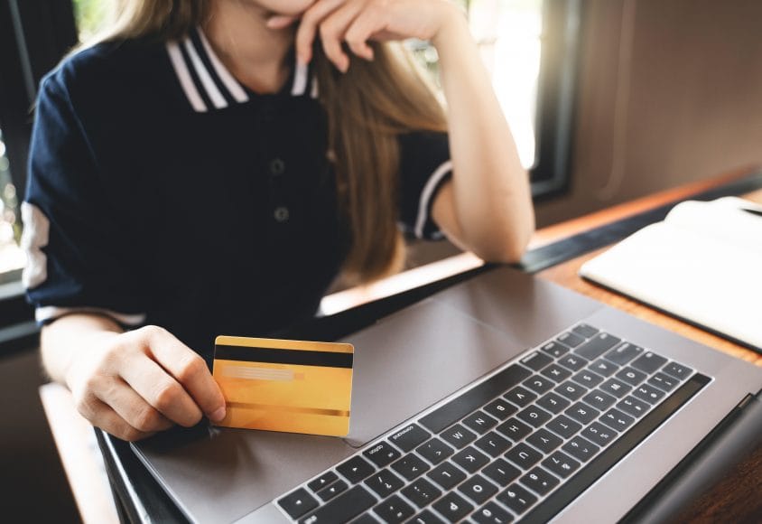 Klientka trzyma kartę płatniczą przy laptopie, symbolizując płatności online w sklepie internetowym.