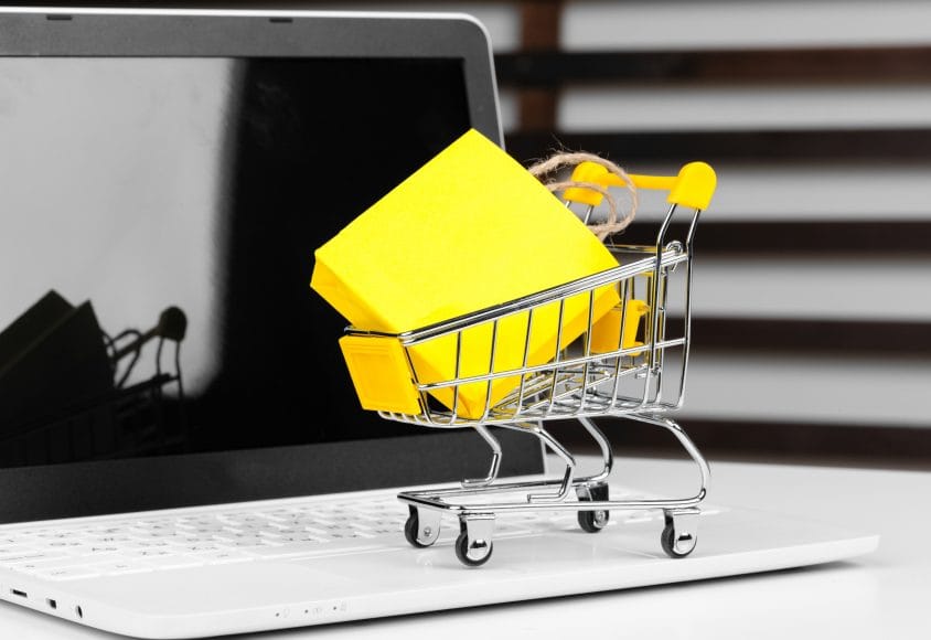 Obrazek pokazujący koszyk z produktem na tle laptopa, symbolizujący stany magazynowe w sklepie online.